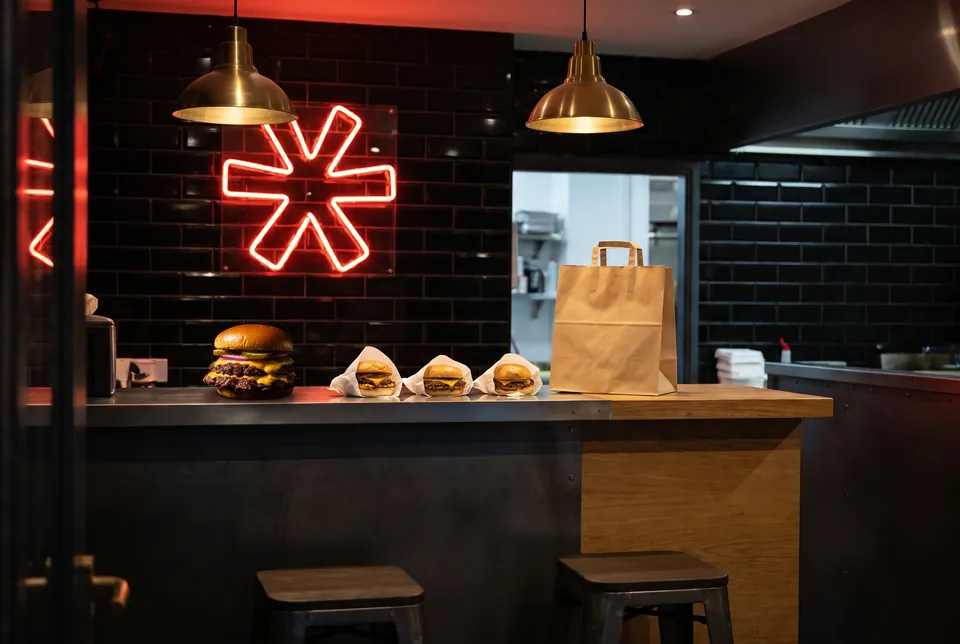 Le comptoir du restaurant le soir : burgers emballés prêts à partir, néon rouge en forme d'étoile